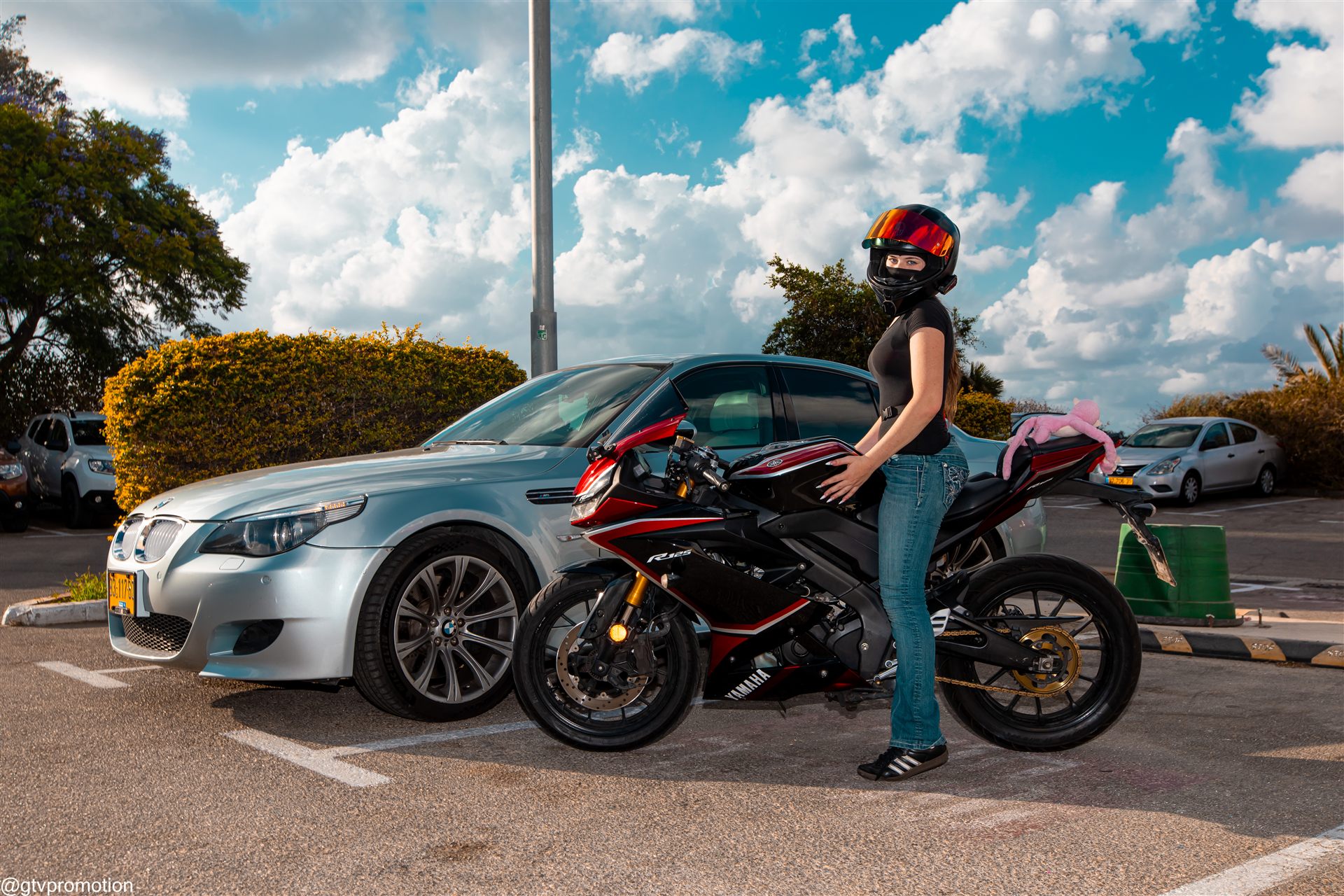 רוכבת עם קסדה לצד ימאהה R125 אדום ושחור ו־BMW M5 כסופה במפגש שפיים