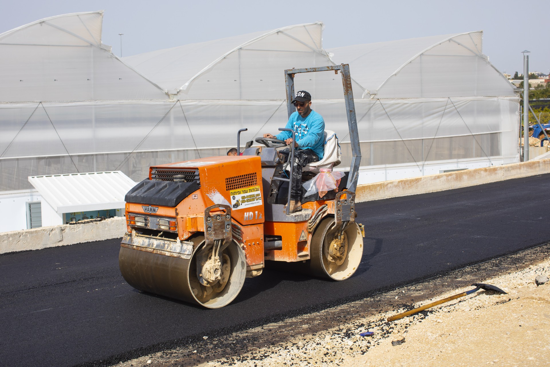 מפעיל מכבש כתום מהדק אספלט שנפרס בעבודות אריאל סחר