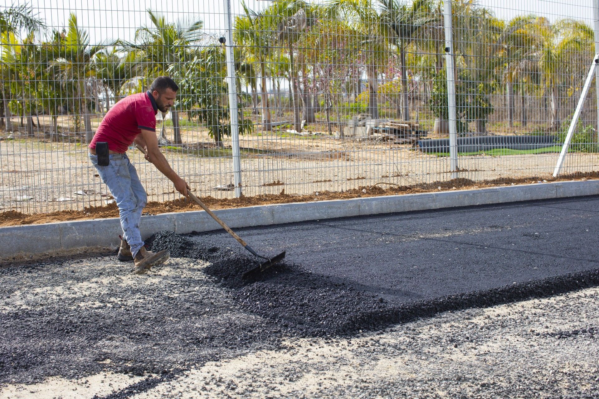 עובד מיישר אספלט ידנית לצד אבן השפה בעבודות אריאל סחר