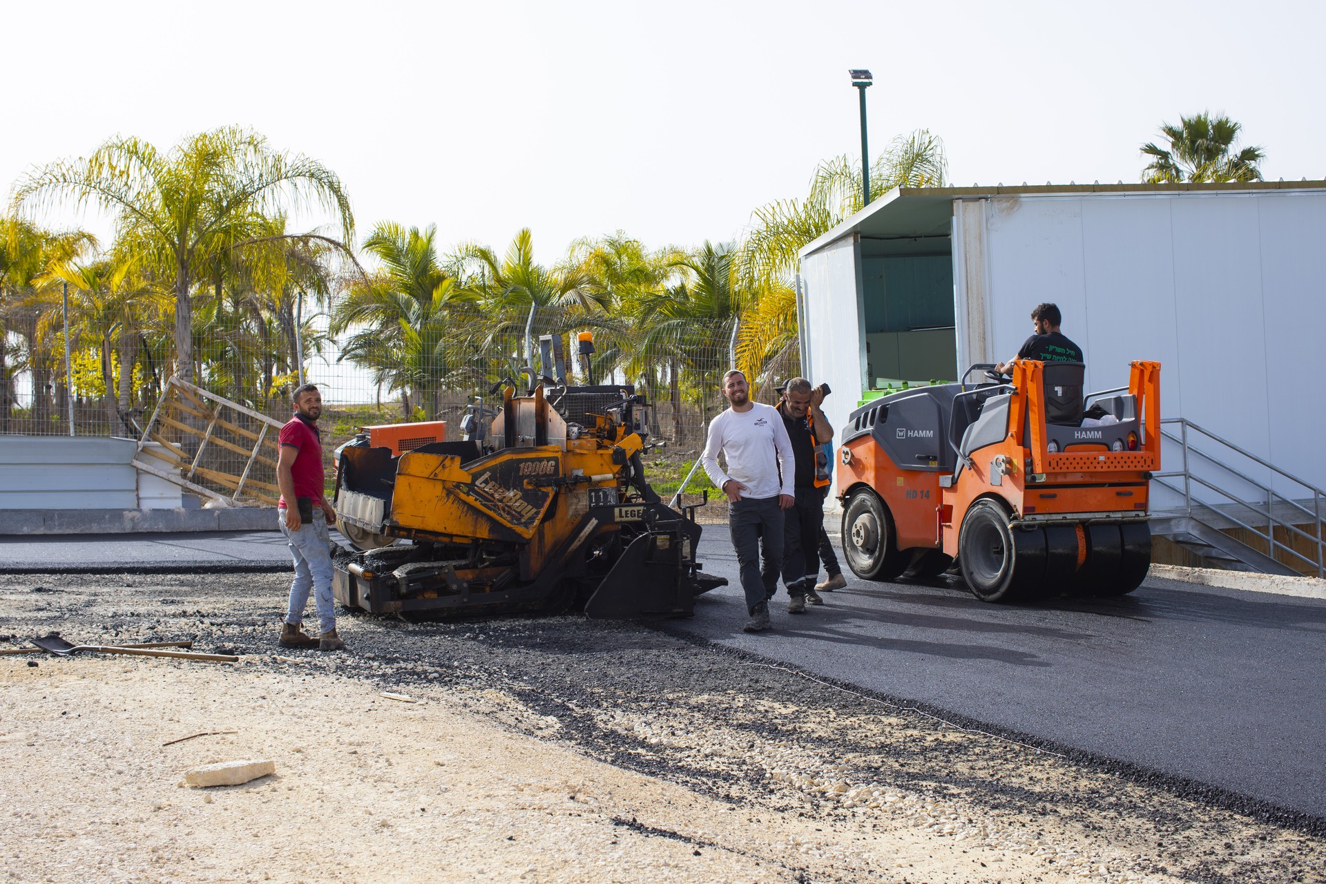 צוות אריאל סחר לצד מכונת סלילה ומכבש על משטח האספלט