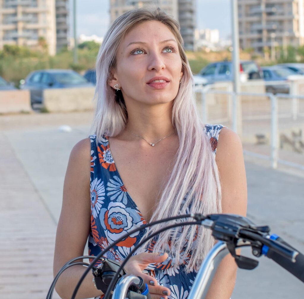 Portrait of a woman with blue eyes and pale blonde hair looking upward beside her bicycle.